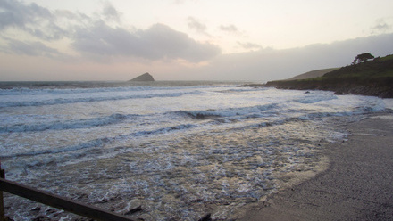 Landscape photgraph of the shore and beach with the waves crashing around a rocky island